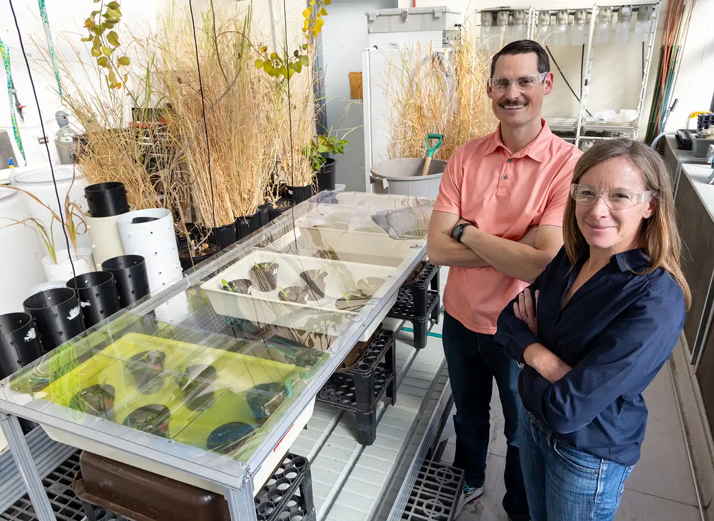 Two people standing near a table where plants grow in individual pots.
