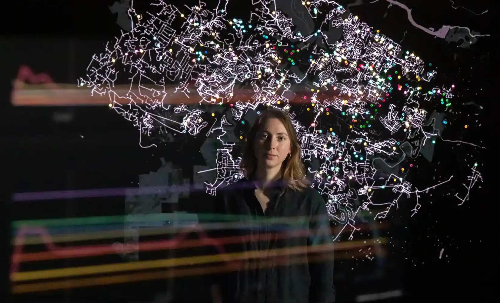 Researcher stands in front of an energy grid map showing energy reliability and impact to services during a cyber attack simulation.