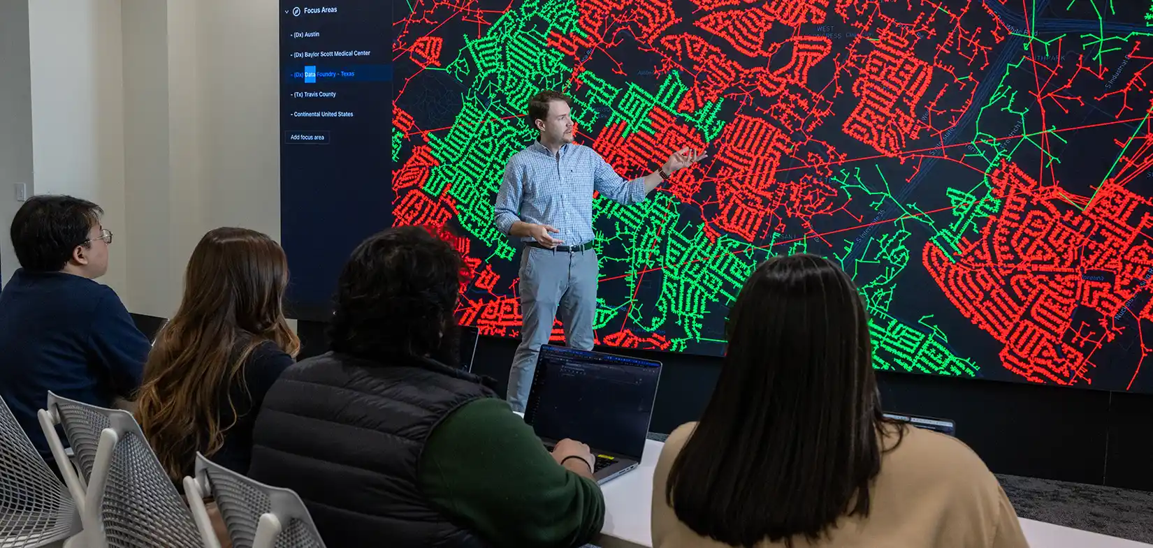 Person pointing cyber data on large display screen in front of audience.