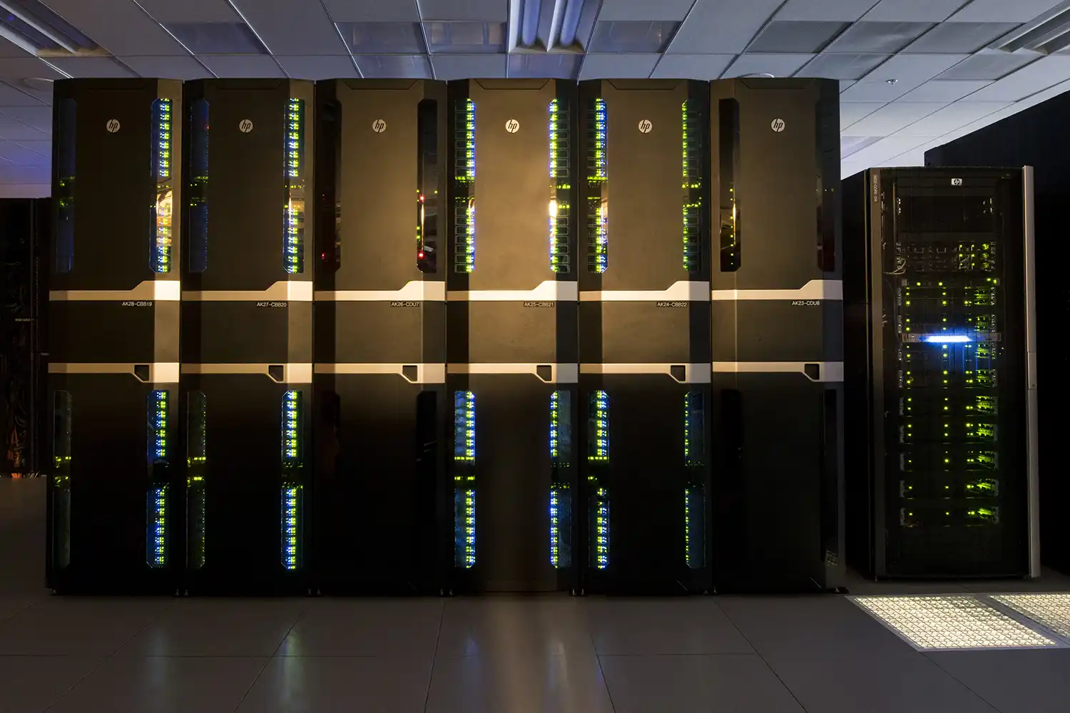 A row of large black server racks with illuminated indicator lights in a data center room.