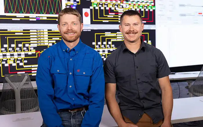 Two people smiling as they stand in front of data visualizations.