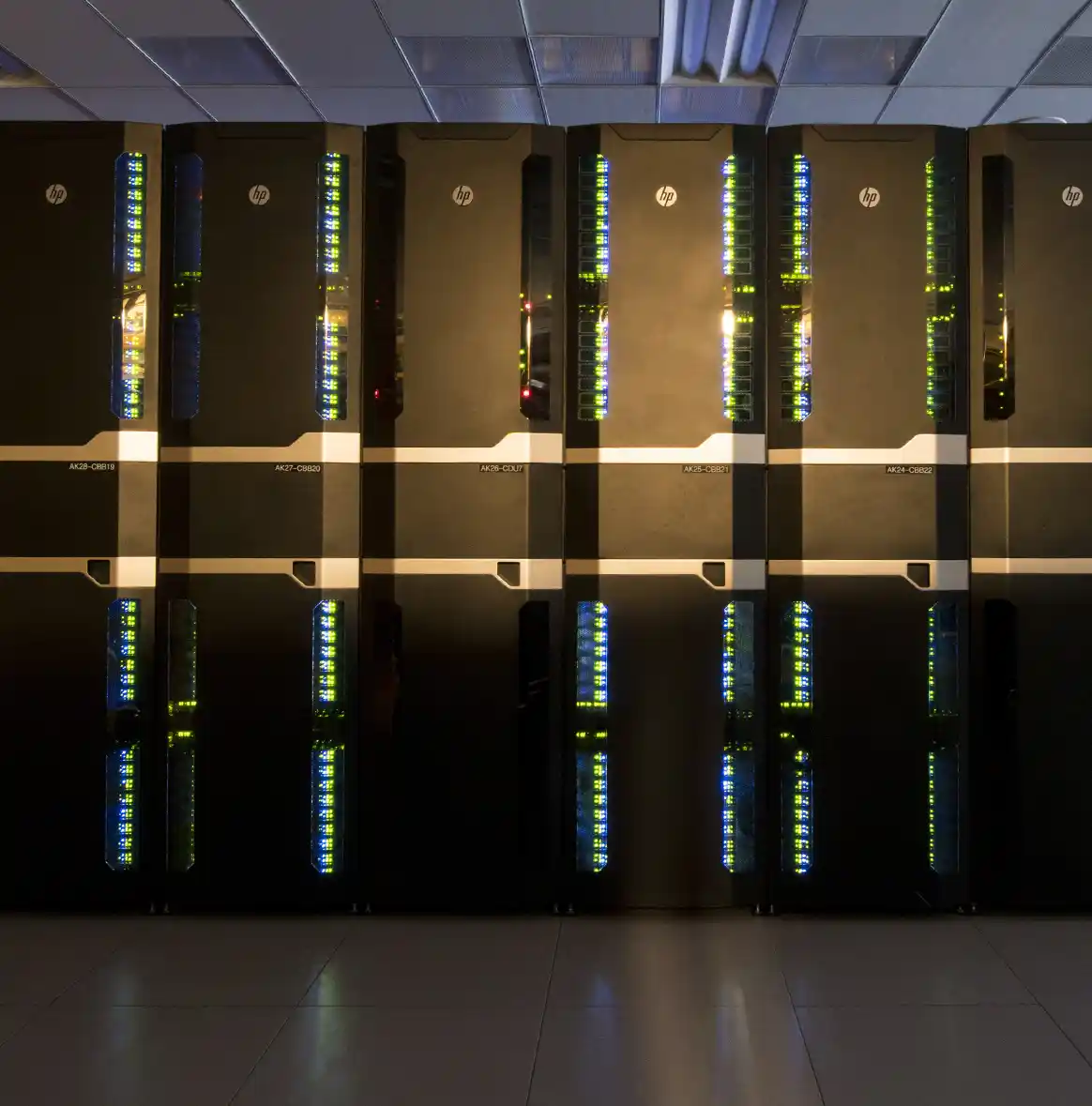 A row of large black server racks with illuminated indicator lights in a data center room.