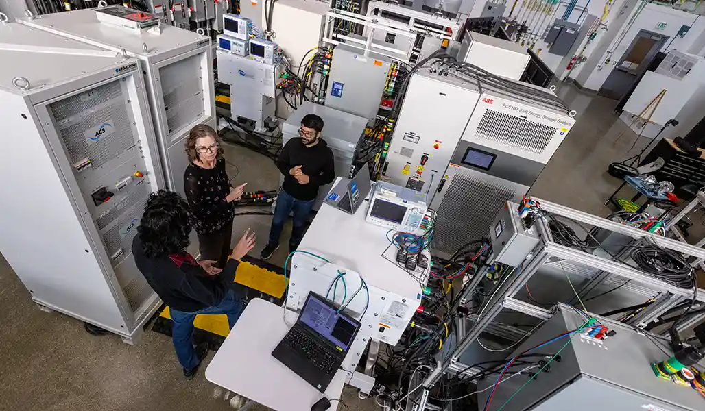 Three people stand in a room of large white cabinets with electrical cords.