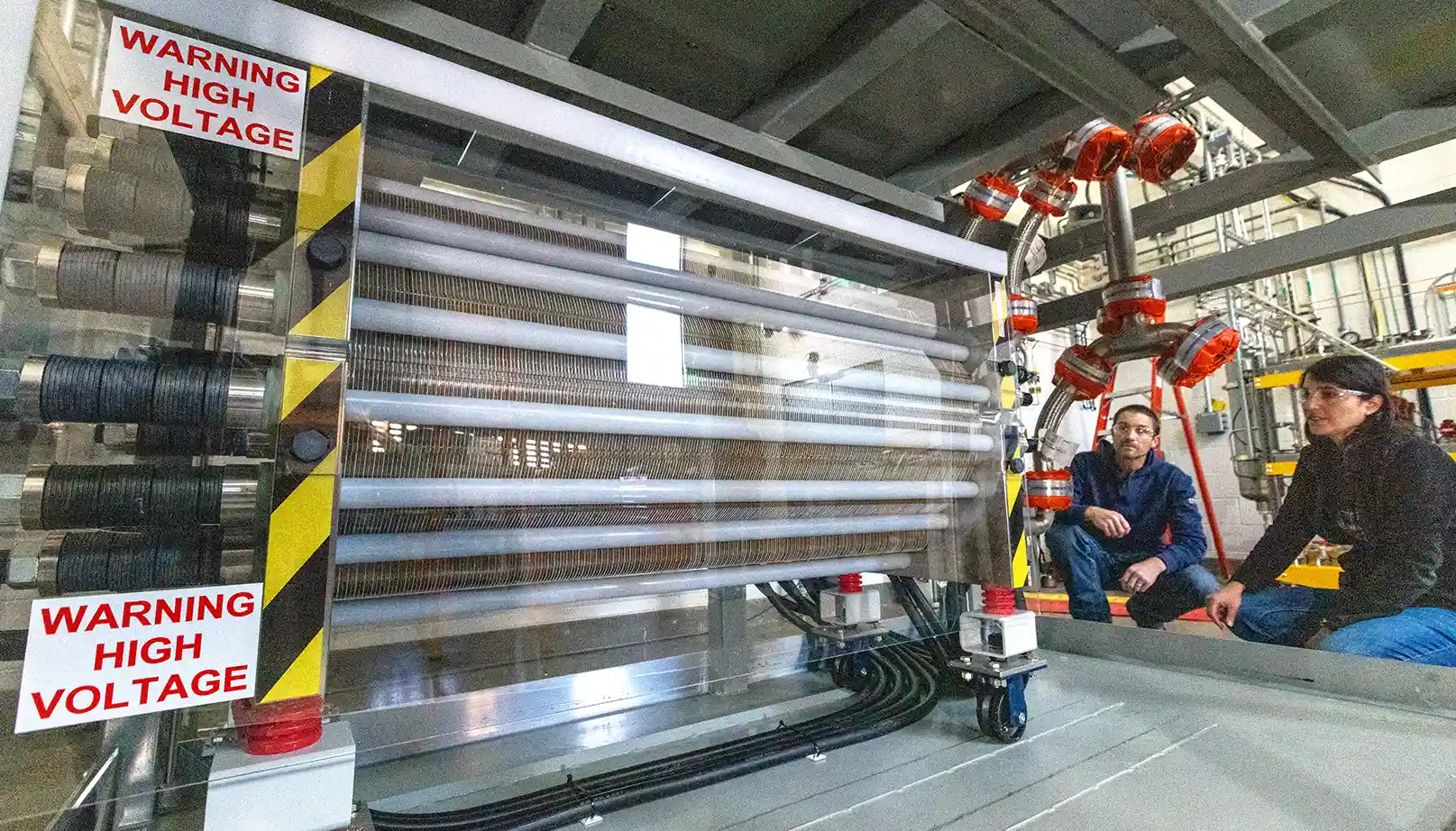 Machinery in the foreground with two people crouched behind.
