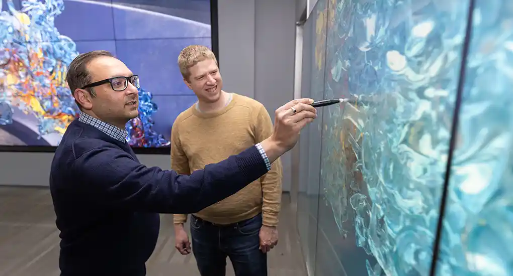 Two men look at swirling colors on a screen.