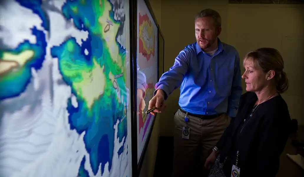 Two researchers look at maps displayed on a large screen