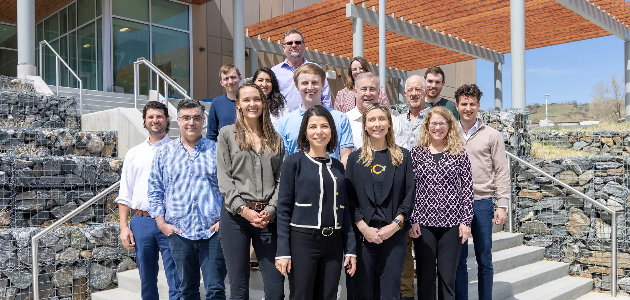 Fifteen people pose for a photo on the steps in front of a building.