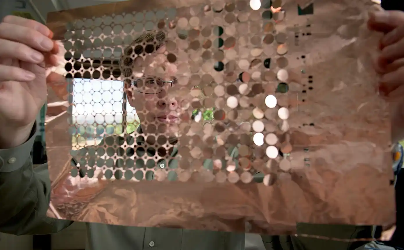 A person holds up a sheet of copper discs.