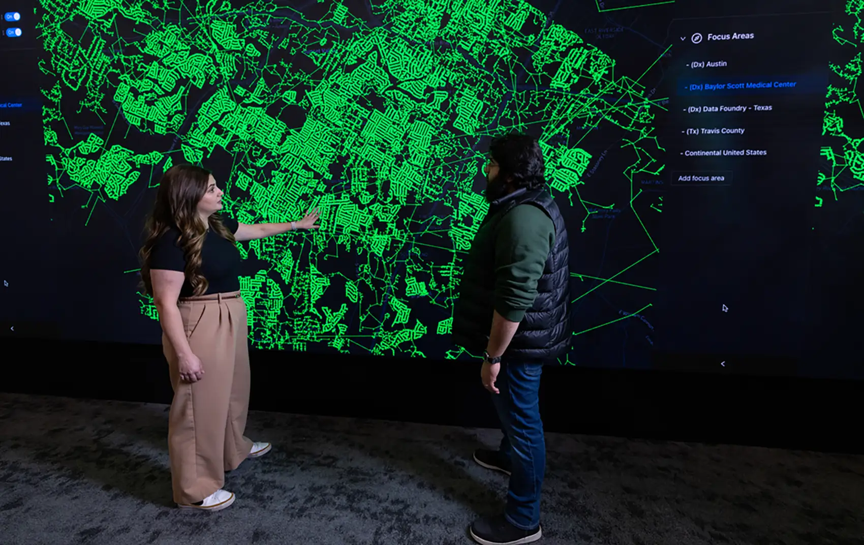 Two people stand in front of a map displayed on a full-wall screen.