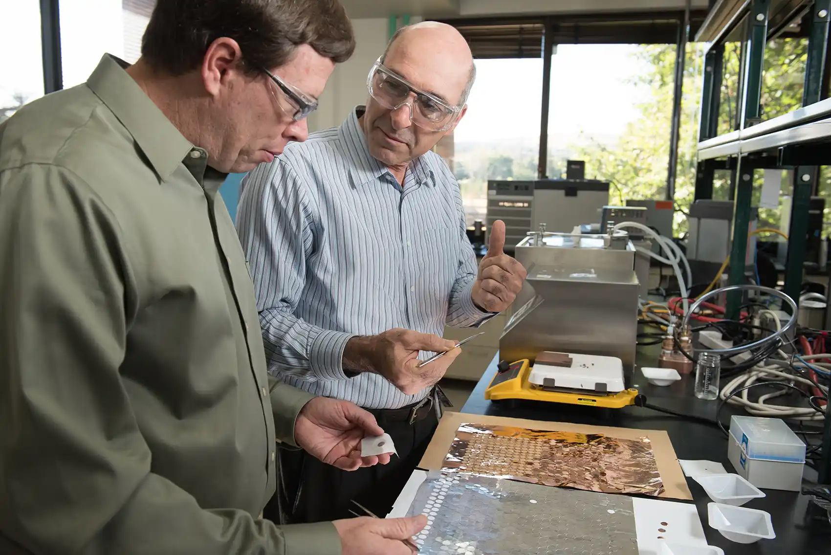 Two people examine a sheet of metal discs in a lab.