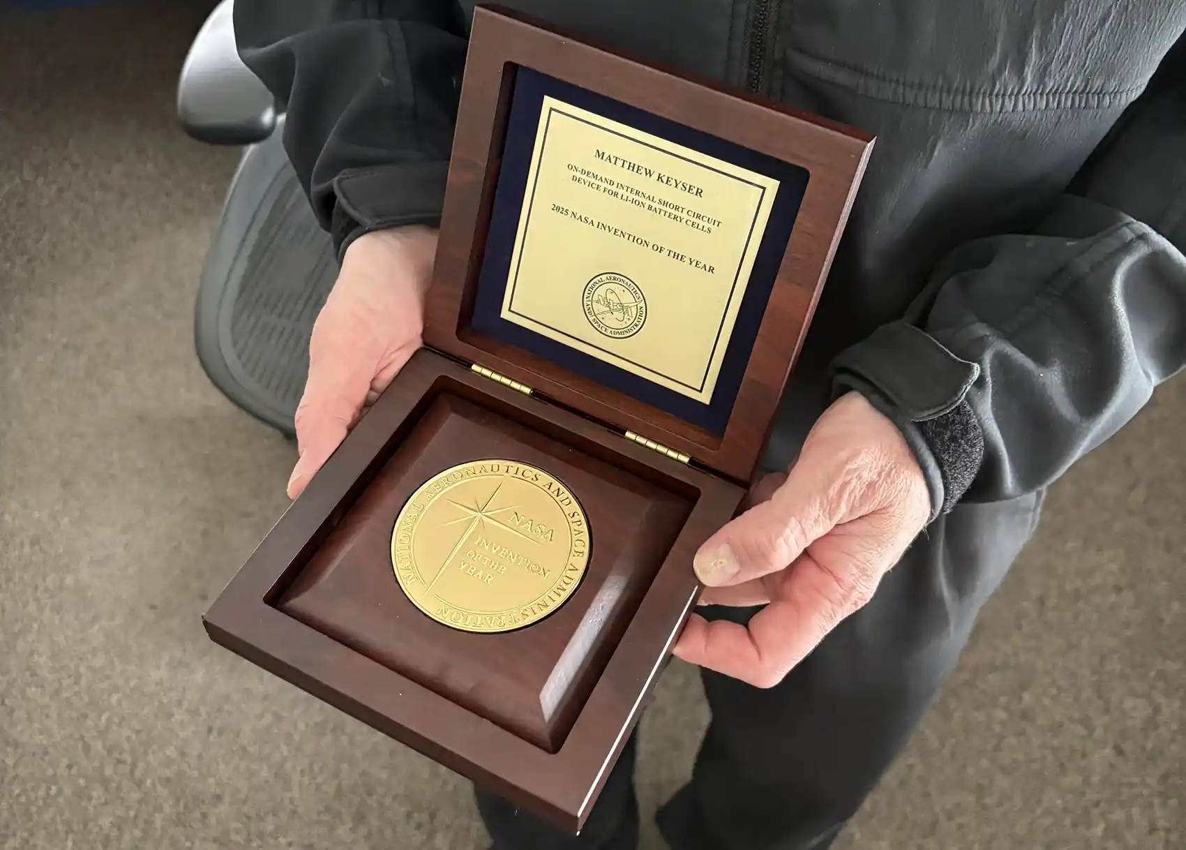 A pair of hands holding a wood box with an award inside.