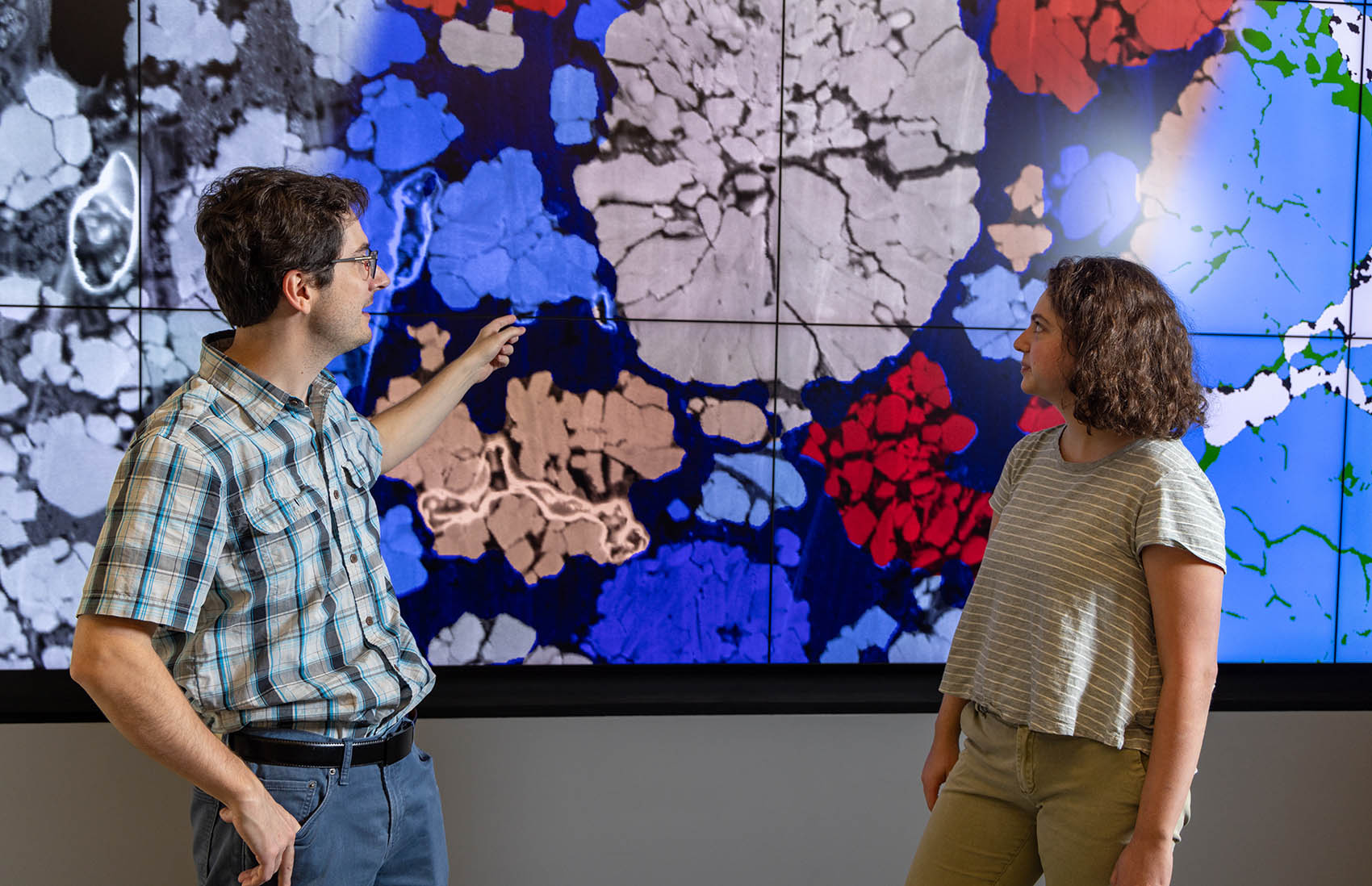 Two people point and look at an image on a large screen.