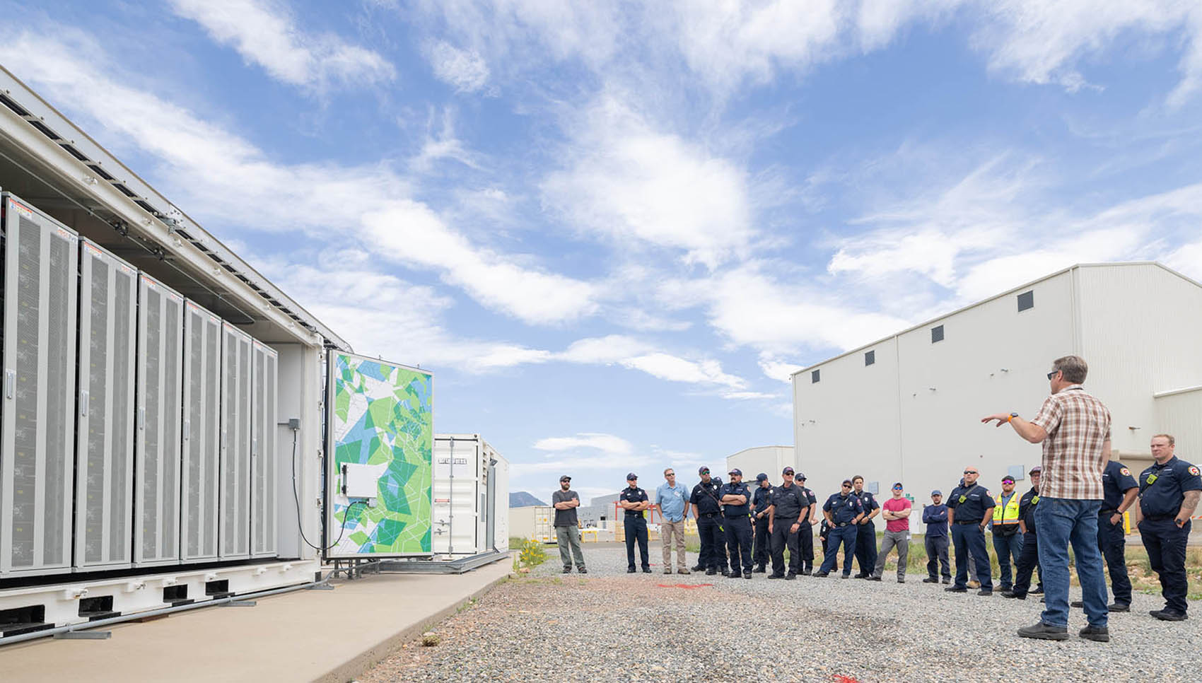 20260625-cradle-to-crisis-approach-improves-battery-safety-and-performance-06232-2 A group of first responders stand outside next to a battery energy storage system.