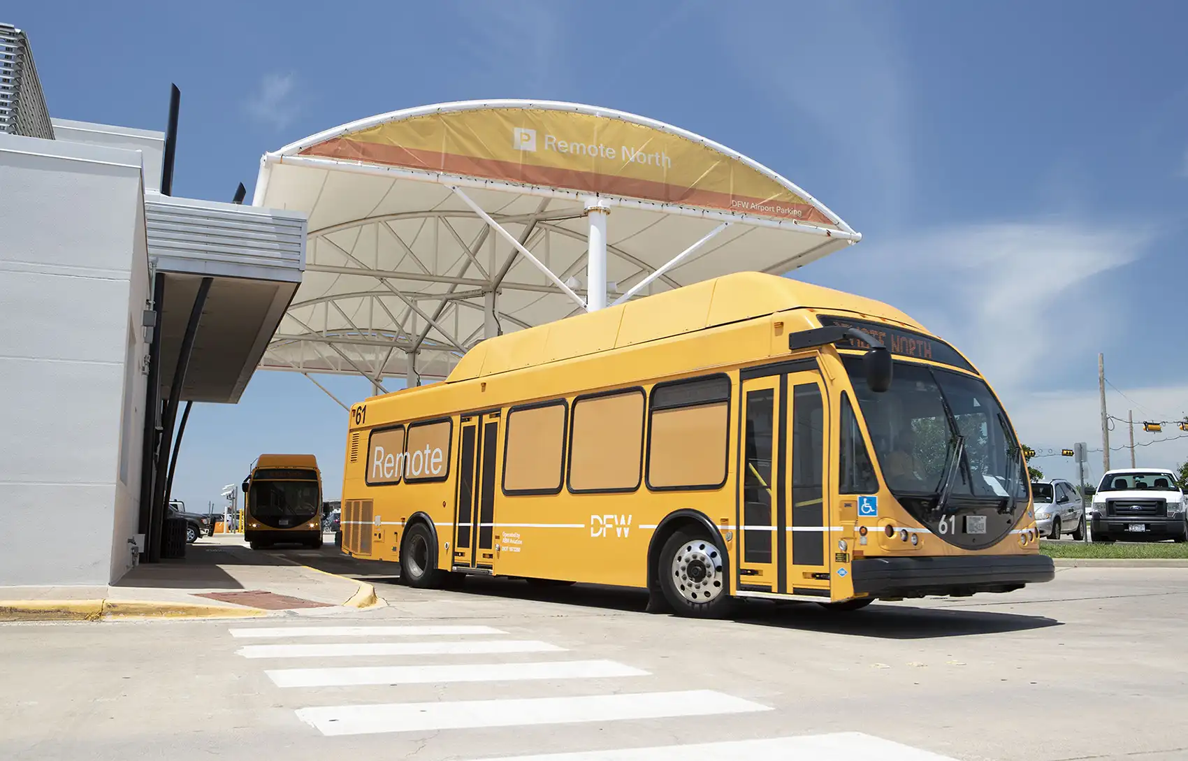 Two large yellow shuttle buses with Dallas Fort Worth International Airport branding park under an airport awning.