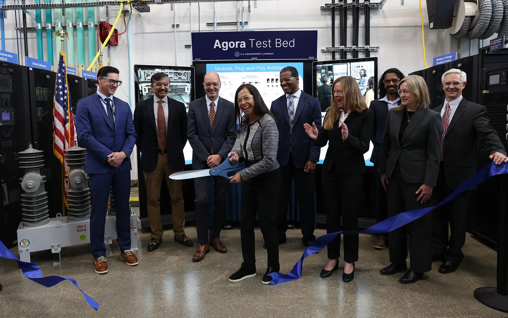 Eight people smile as a person cuts a ribbon with giant scissors.
