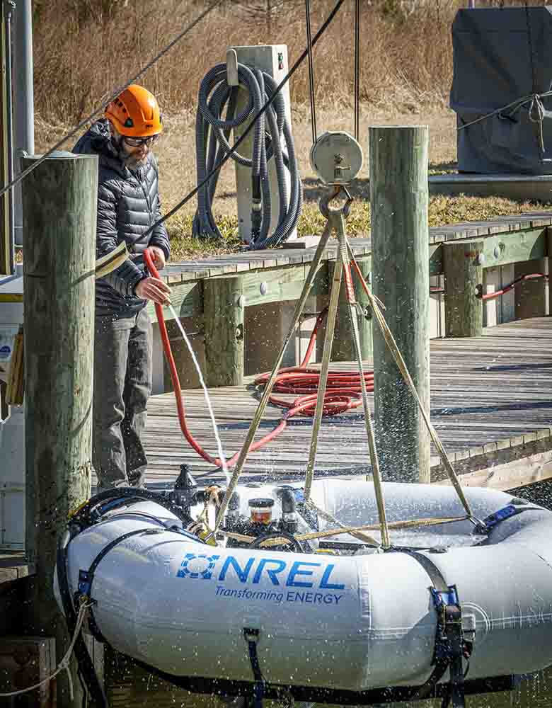A researcher in a hardhat stands on a dock and lowers a desalination device, which has 