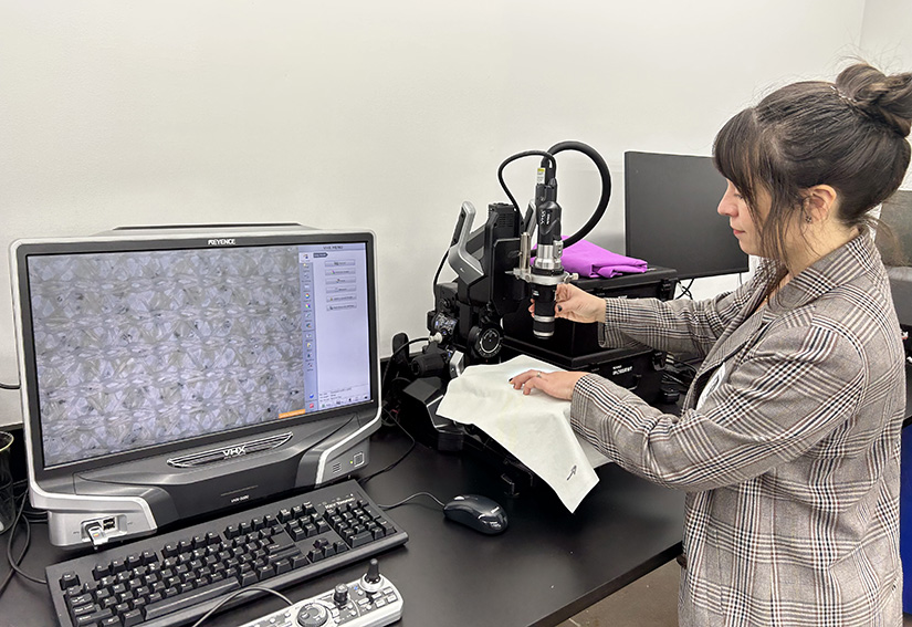 A person works on a microscope next to a computer. 