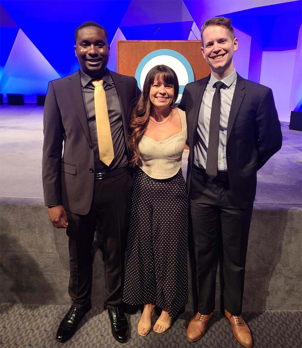 Three people stand close together and smile in front of a podium. 