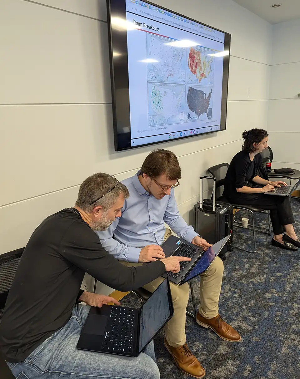 Three people are seated while working on laptops
