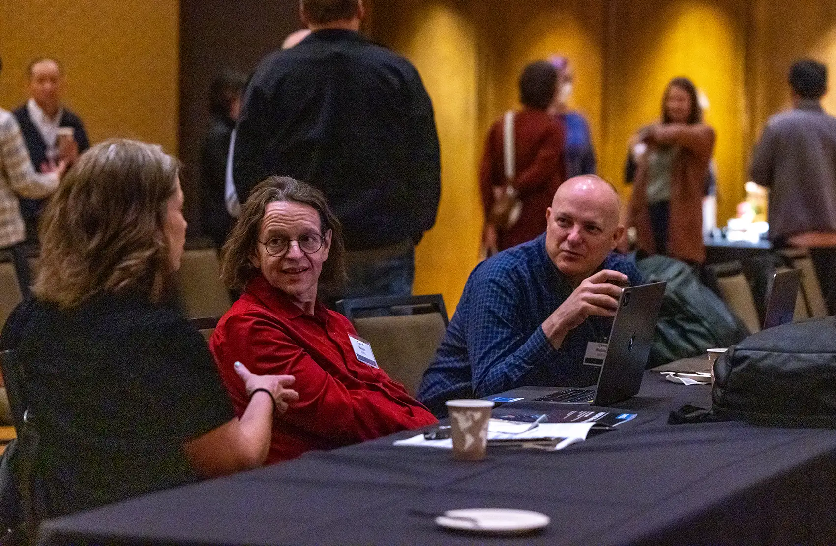 Three attendees engage in focused discussion while sitting at a table in the workshop hall.