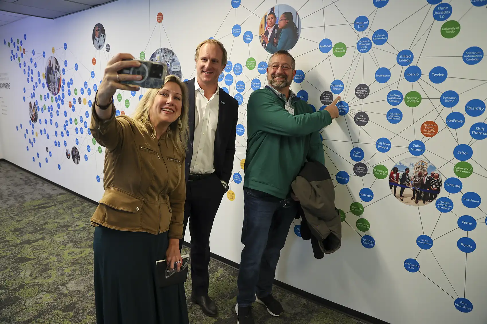 Three people pose for a selfie in front of a wall with graphics on it.