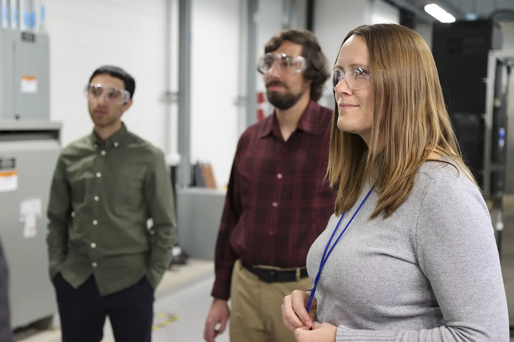 Three people wearing safety goggles stand in a lab.