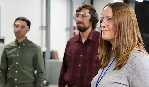 Three people wearing safety goggles stand in a lab.
