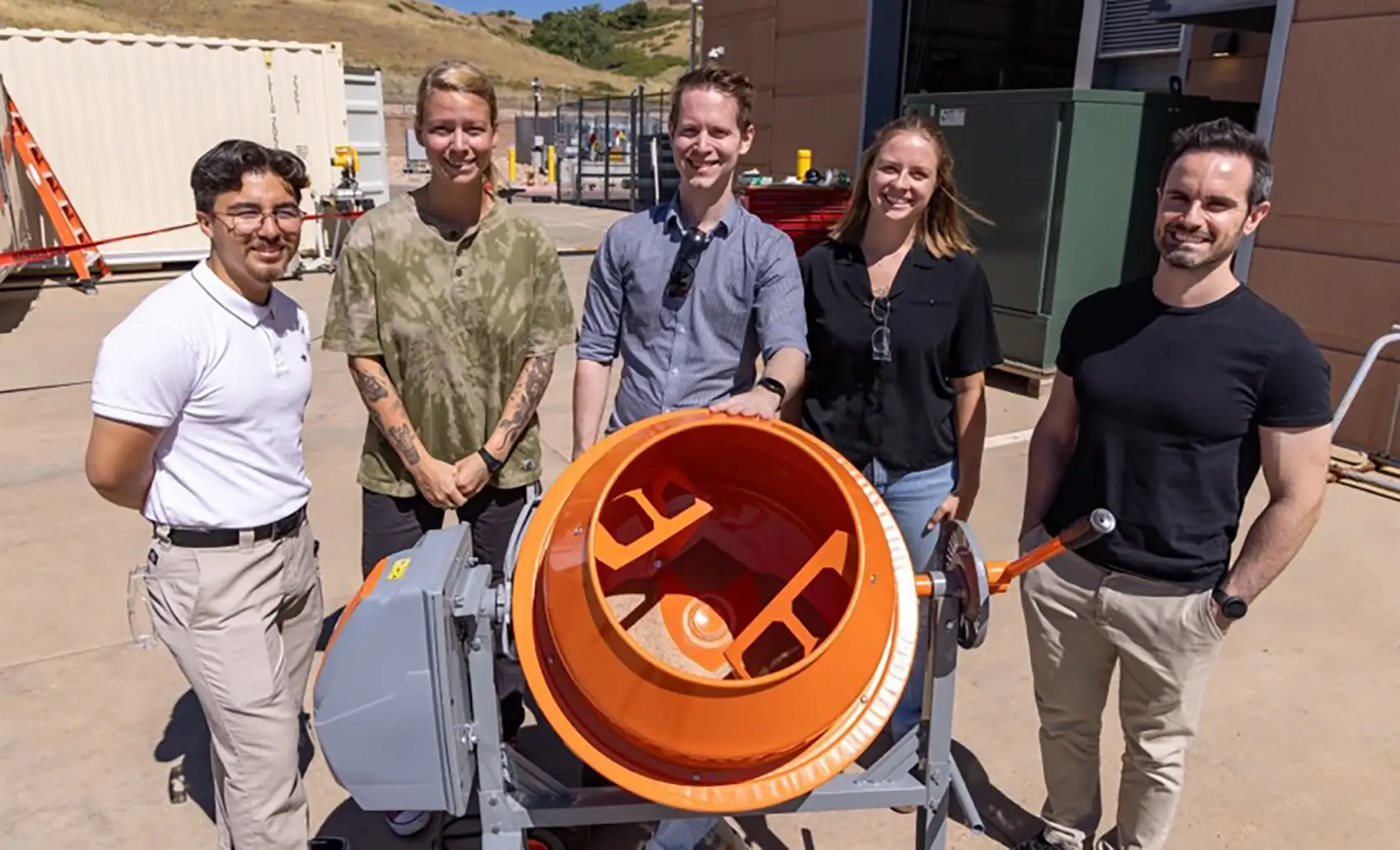 Five people standing outside behind a scooter-sized cement mixer.