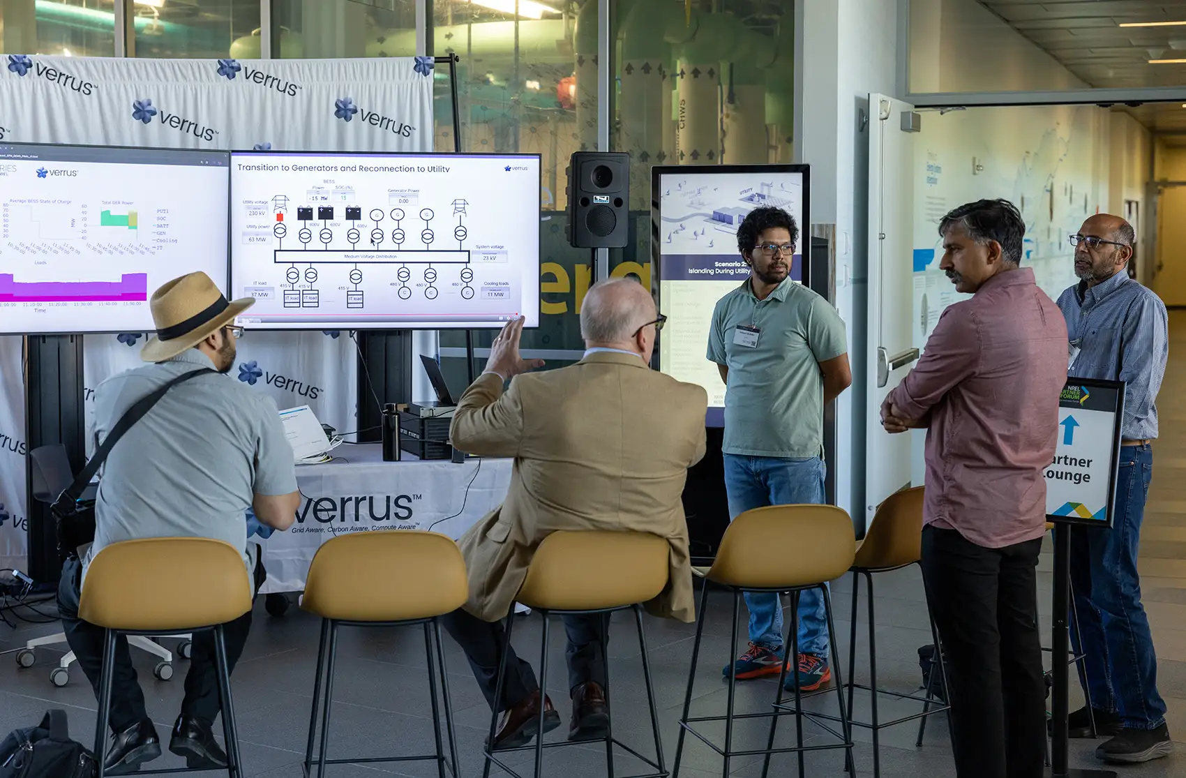 20260226-could-a-new-kind-of-data-center-give-back-to-grid-99636 Five people conversing in front of a table reading “Verrus” and screens displaying data