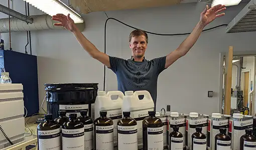 Continue reading about Evan raises his arms, palms down, over a collection of containers with the name, “Zila Bioworks” written on them.