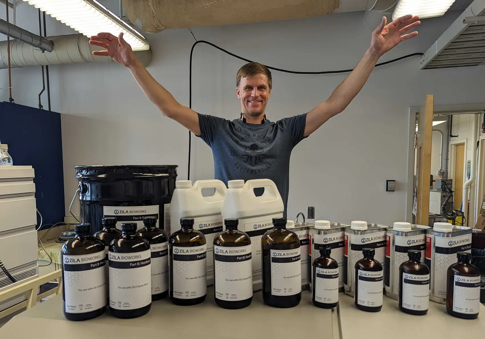 Evan raises his arms, palms down, over a collection of containers with the name, “Zila Bioworks” written on them.