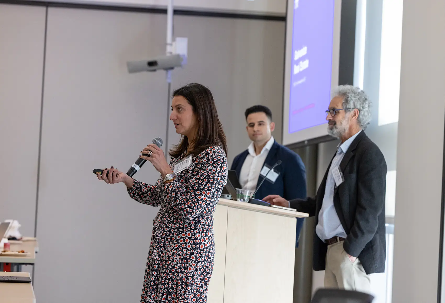 Three people stand around a podium while one speaks into a microphone.