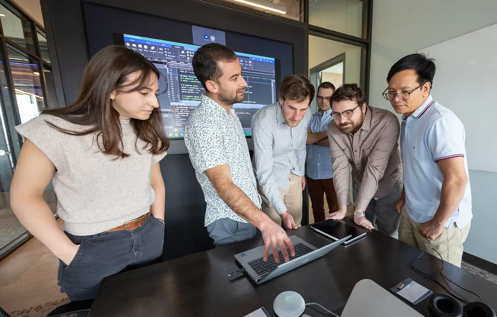 Six people stand around a computer.