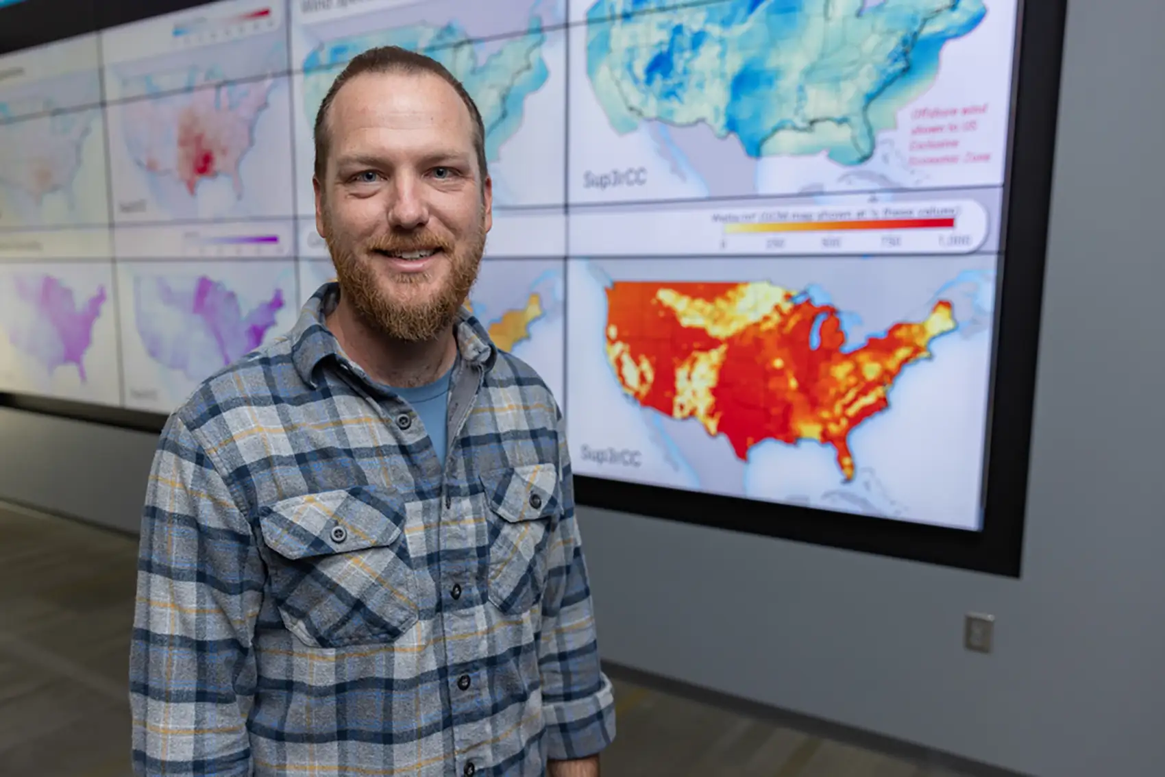 Ryan King in front of a wall of screens with maps of the United States on them.