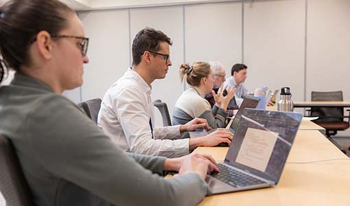 Five people seated at a conference room table while using laptop computers