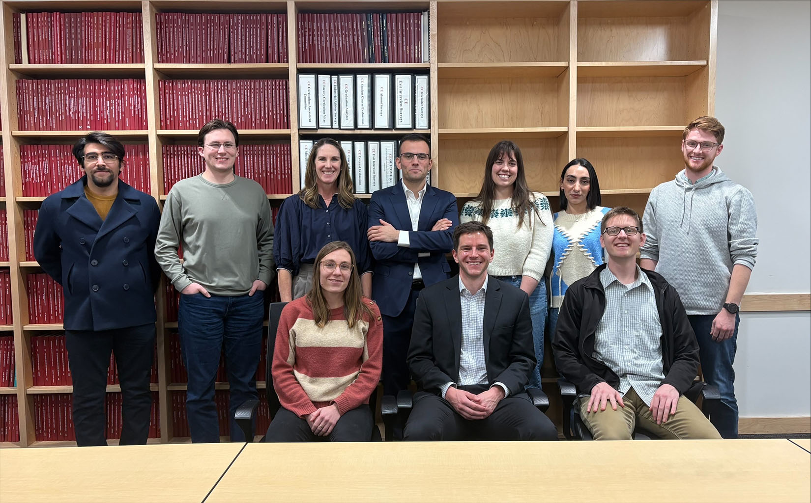 10 people posing in front of a large wall bookcase