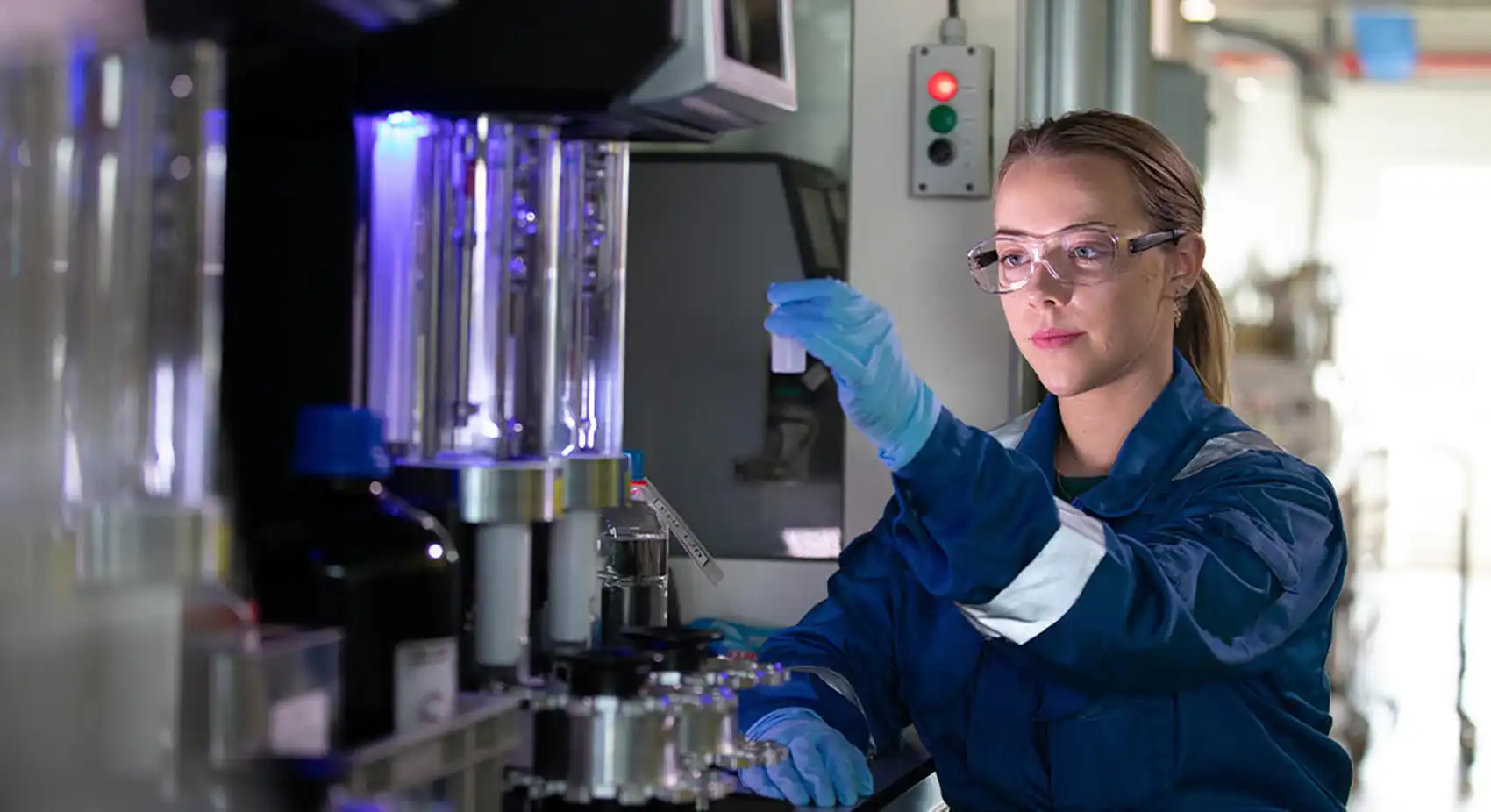 A person wearing gloves and safety goggles holds up a container in a lab.