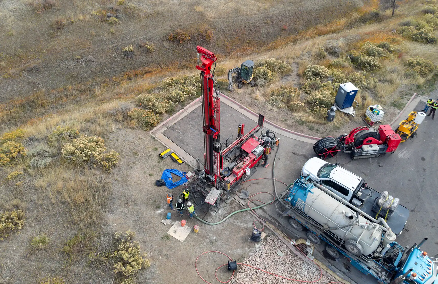 20260727-the-fast-lane-3-ways-geothermal-companies-can-get-more-heat-102168 An aerial view of people in reflective vests and hard hats standing near drilling equipment and trucks