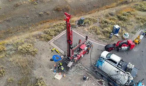 Continue reading about An aerial view of people in reflective vests and hard hats standing near drilling equipment and trucks