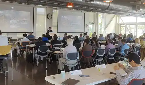 A room full of people in chairs facing a person giving a presentation.