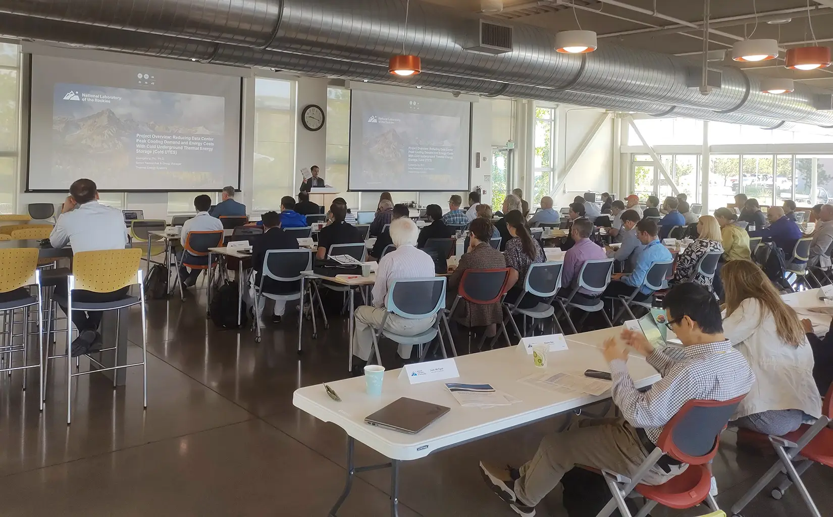 A room full of people in chairs facing a person giving a presentation.