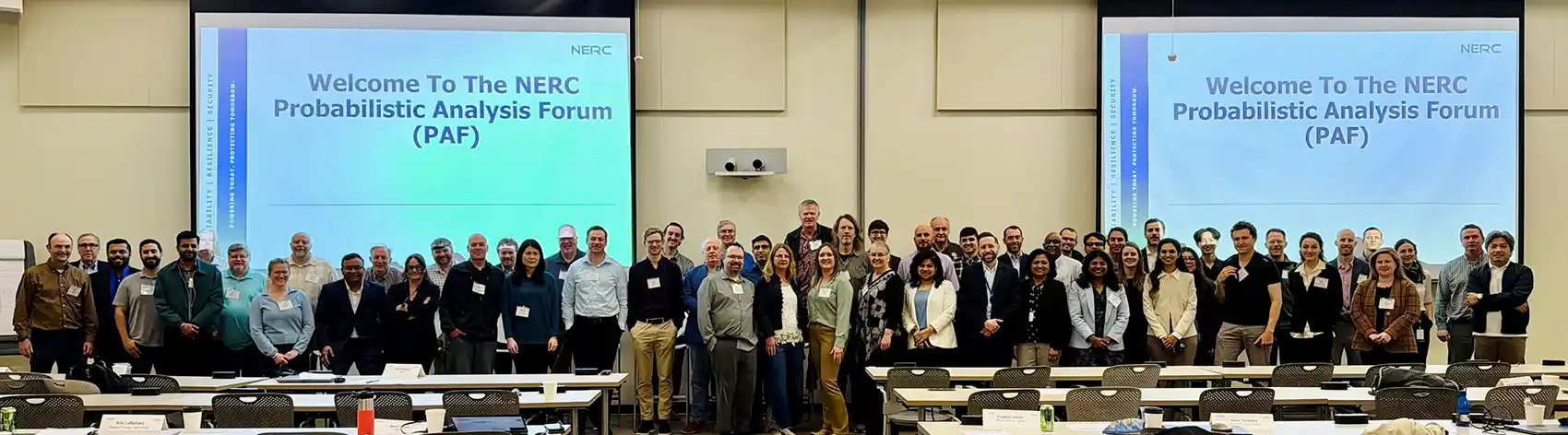 20260818-nlr-and-north-american-electric-reliability-corporation-launch-partnership-to-advance-north-american-grid-reliability-paf A large group of people posing in front of two screens with the text Welcome to the NREC Probabilistic Analysis Forum (PAF)