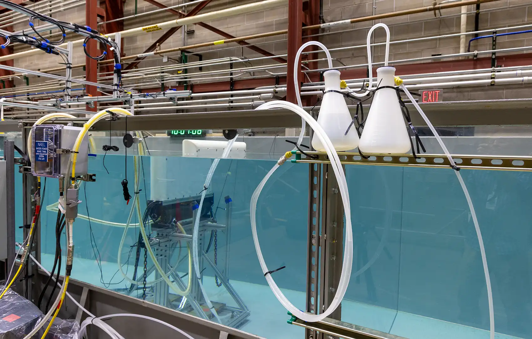 20260914-can-surge-wave-tech-survive-the-open-ocean-094229 Side view through the glass wall of a wave tank in a laboratory showing the underwater testing apparatus inside the tank.