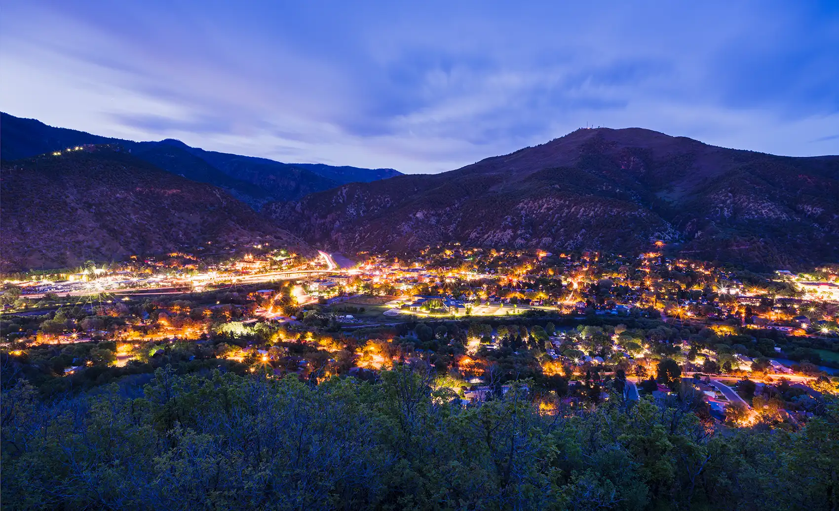 Overlooking town lit up at twilight with mountains in background.