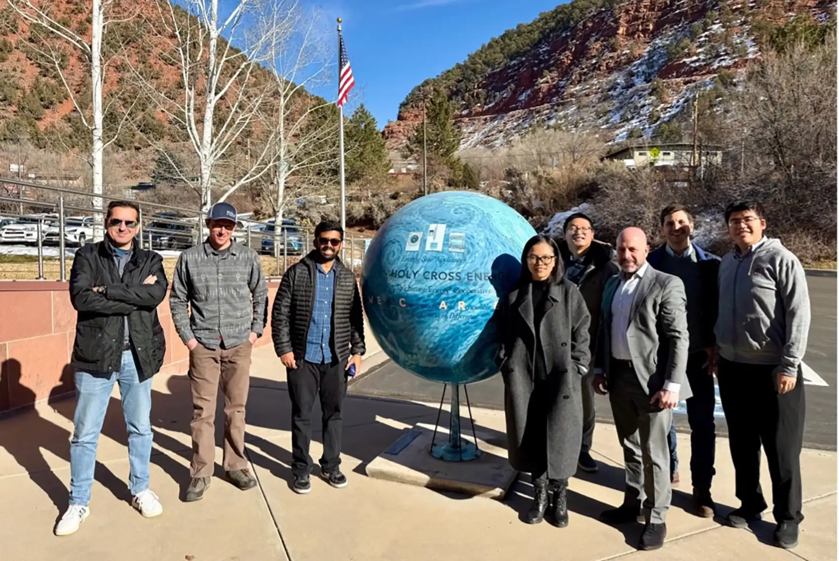 Eight people stand around a giant globe outside.