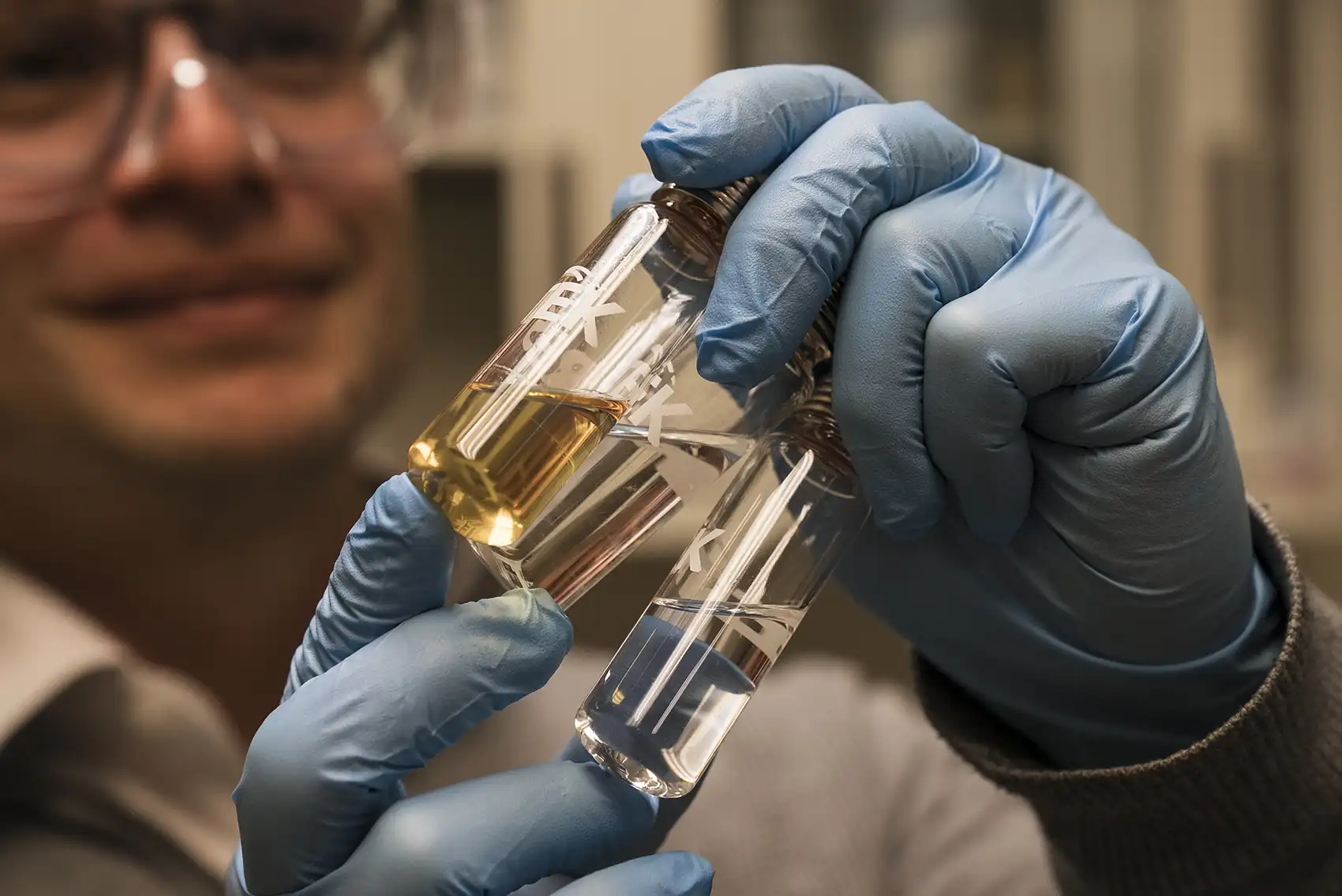 20261013-how-2-startups-are-turning-plant-waste-into-products-alder A person wearing blue gloves holds glass test tubes containing liquid samples.