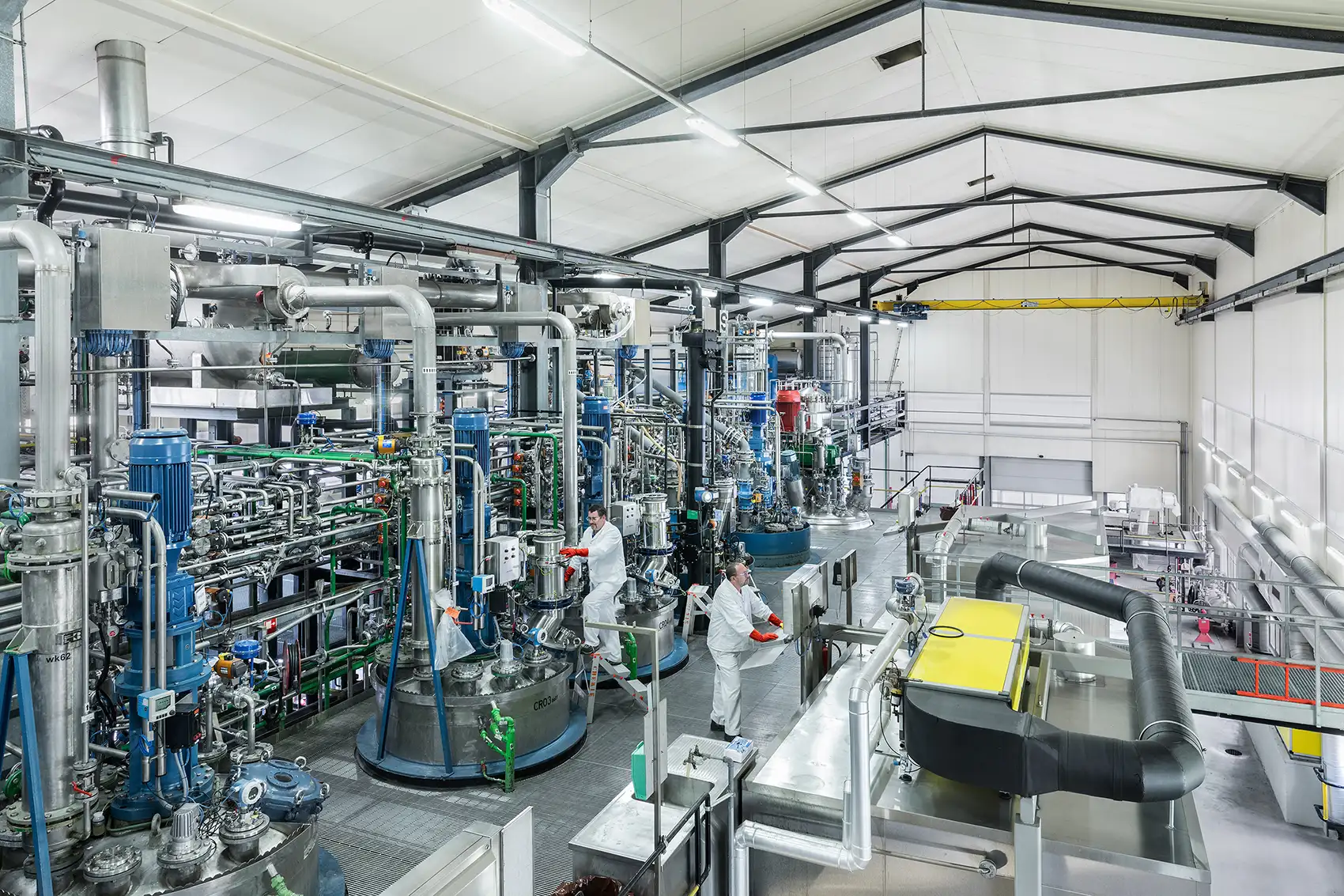 20261030-how-2-startups-are-turning-plant-waste-into-products-bloom Industrial facility with stainless steel pipes, tanks, and processing equipment, with researchers in white protective clothing.