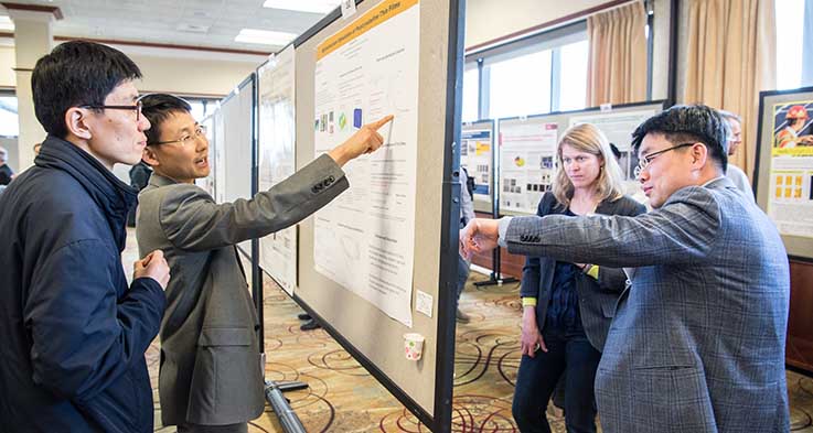 Researchers point to posters on a wall and share presentations with workshop participants.