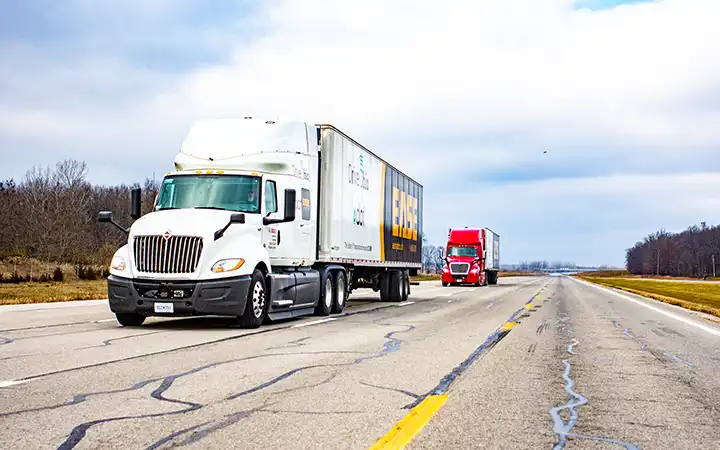 Two people wearing eye protection look at a laptop propped on the hood of an electric vehicle as it charges inside a laboratory.