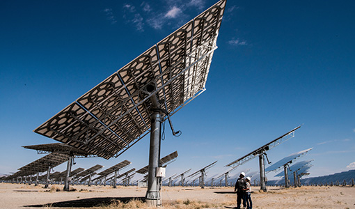 46187-flt Two workers looking underneath a large concentrating solar power array in a desert area.